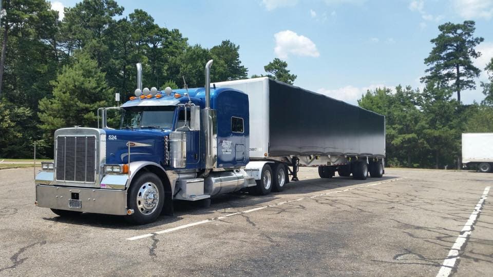 Dark blue Peterbilt semi-truck with a covered flatbed trailer in a parking lot